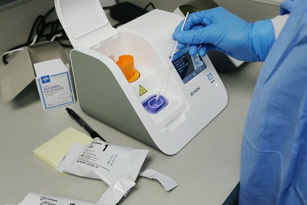 A lab technician using a swab to put a sample into a rapid test machine.