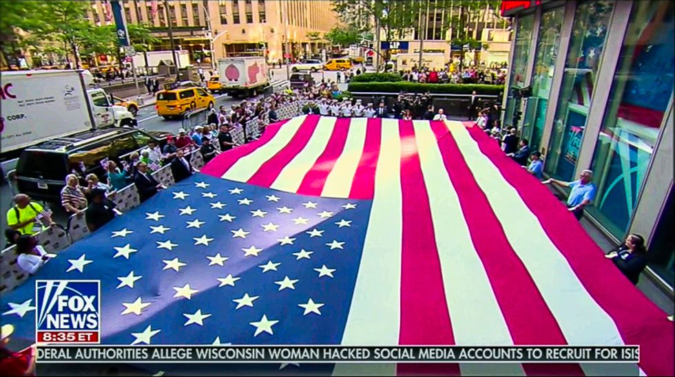 Fox & Friends hosts sit while flag is unfurled and military performs national anthem