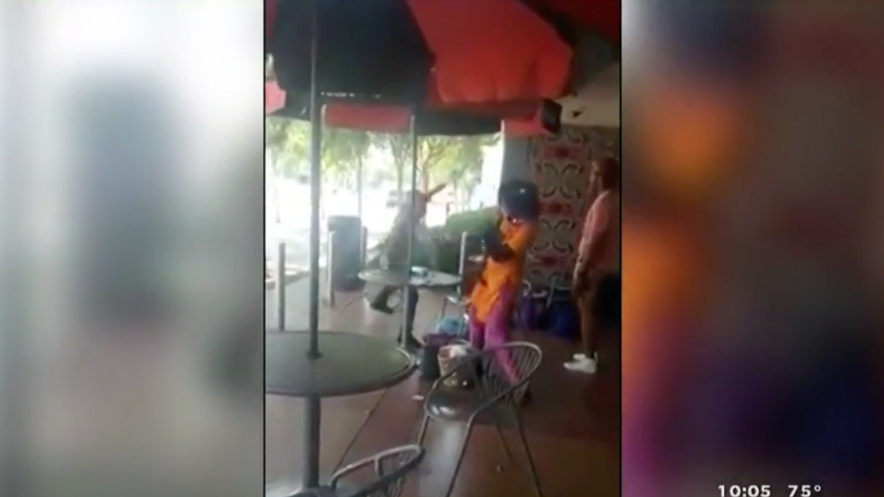 Racist white man caught on camera after throwing a chair at black woman while she's reading outside