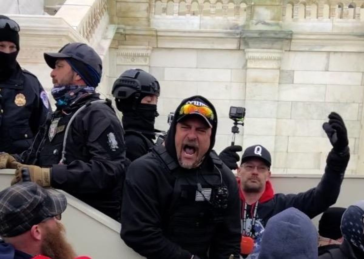 Tim Hart waves to rioters at the Lower West Plaza as Michael Flynn associate Brian Gamble looks on and Proud Boy James Hoel speaks with a Capitol police officer.