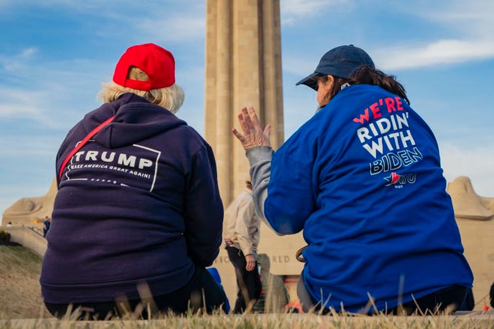 Two women conversing with their backs to the camera, one wearing a Trump shirt and the other a Biden shirt.