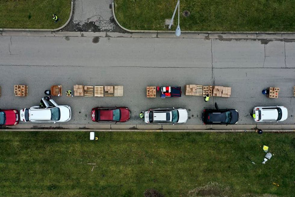 Volunteers load boxes of food into a line of waiting cars.